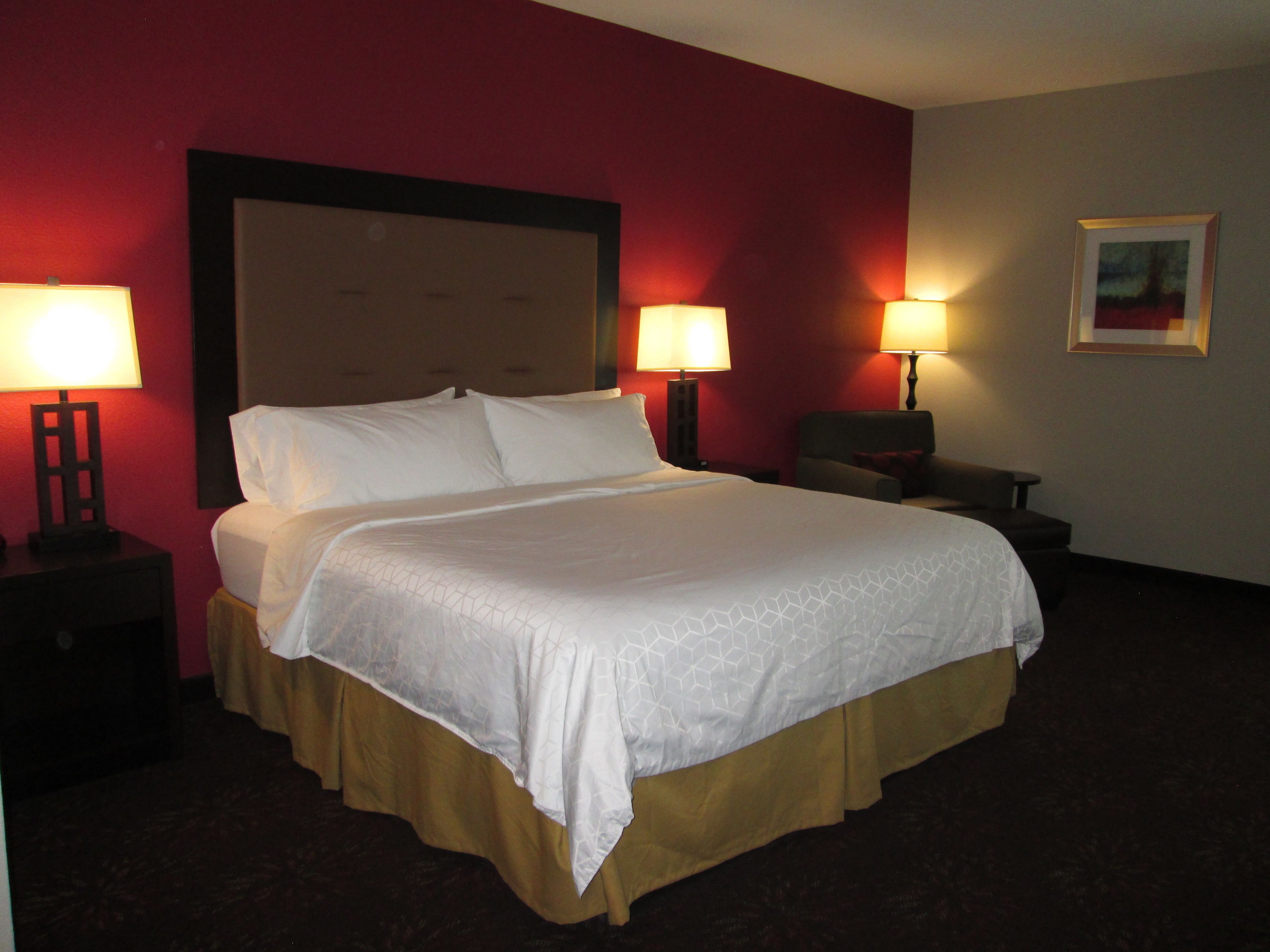 Habitación de hotel con una cama grande, dos lámparas de noche, una silla y un cuadro en la pared.