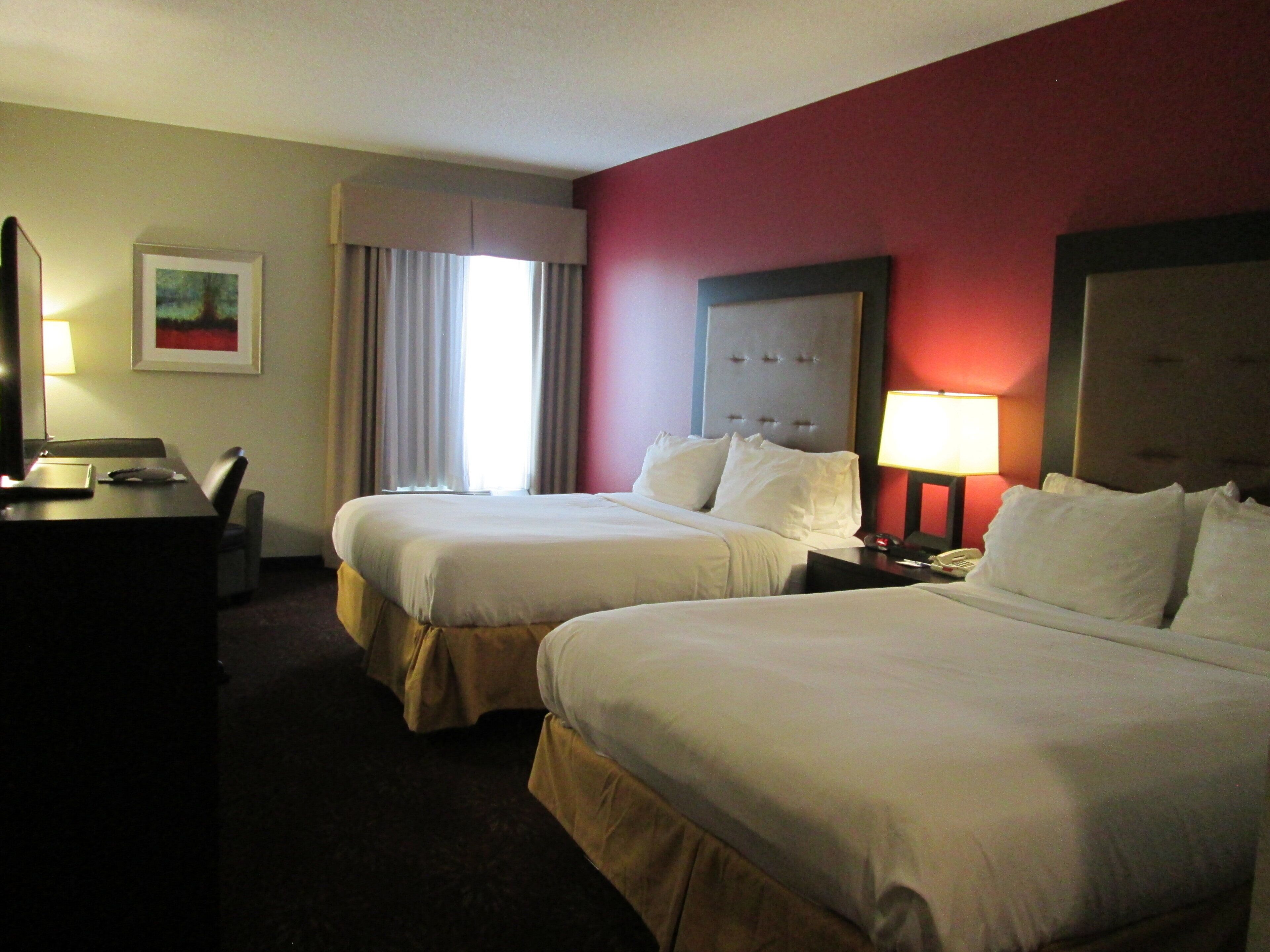 A hotel room with two beds, a desk, a chair, a lamp, and a painting on the wall.