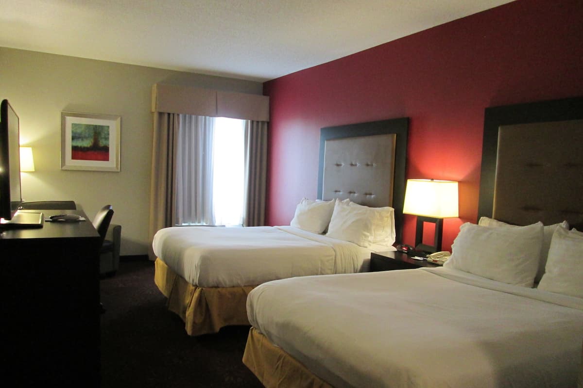 A hotel room with two beds, a desk, a chair, a lamp, and a framed picture on the wall.