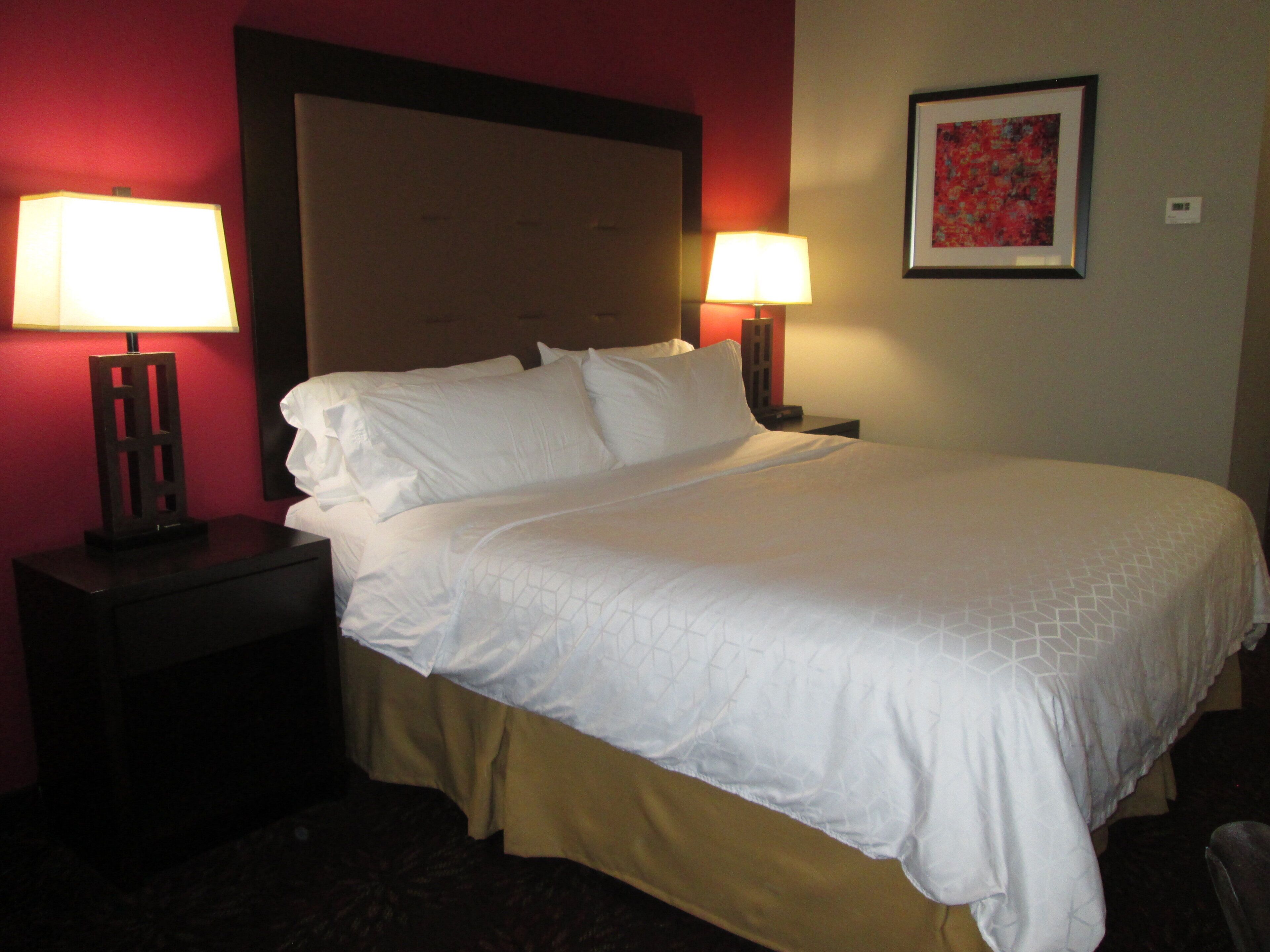 A hotel room with a large bed, two bedside lamps, a headboard, and a framed picture on the wall.
