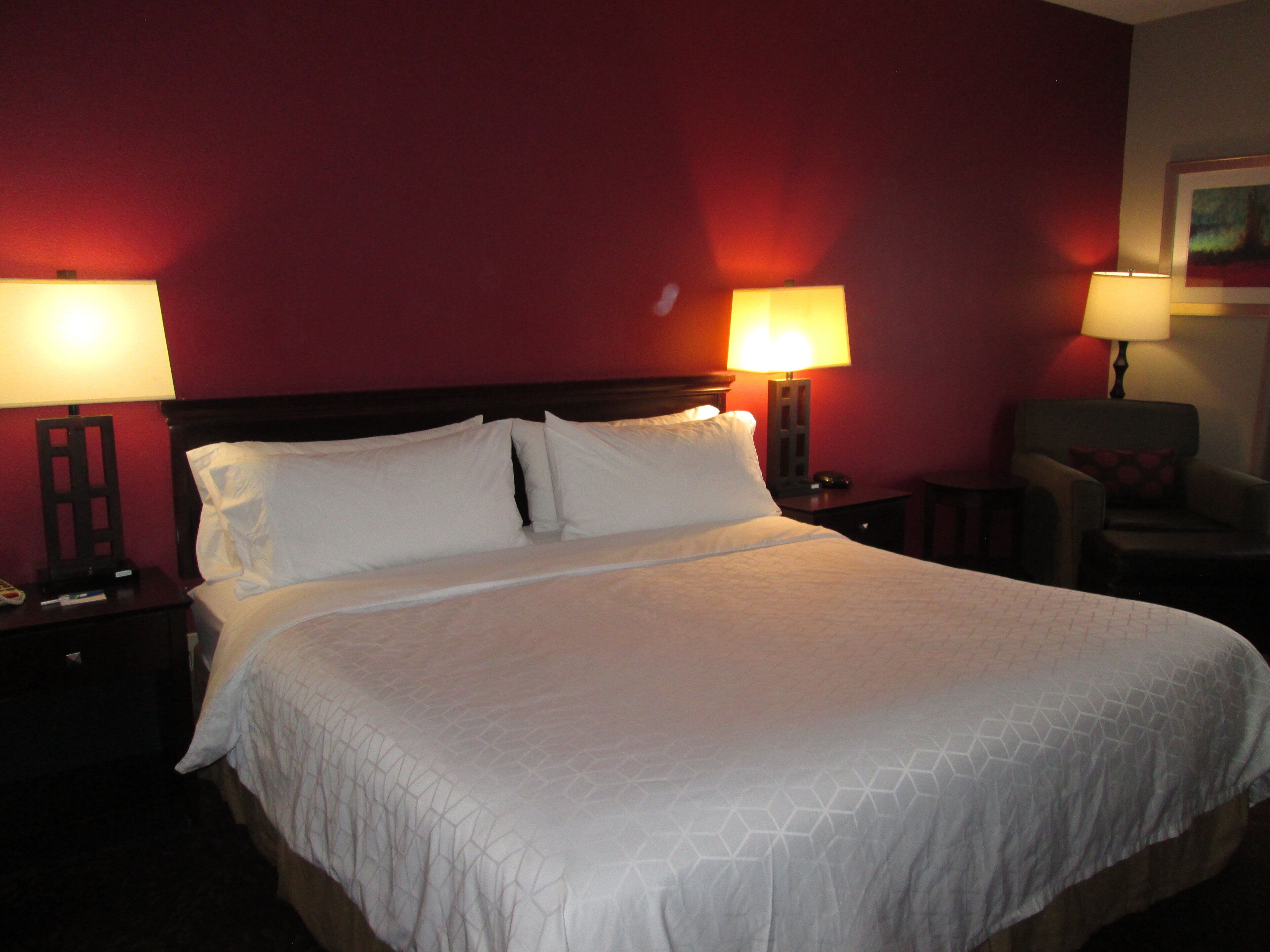 A hotel room with a large bed, two bedside lamps, a chair, and a painting on the wall.