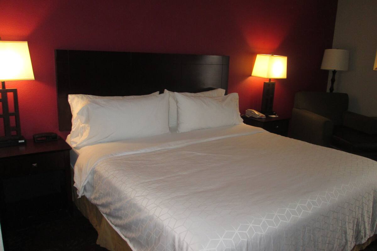 A hotel room with a large bed, two bedside tables with lamps, a chair, and a telephone.