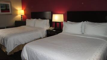 Una habitación de hotel con dos camas, cada una con ropa de cama blanca y cabeceros, una mesita de noche con lámpara y un cuadro en la pared.