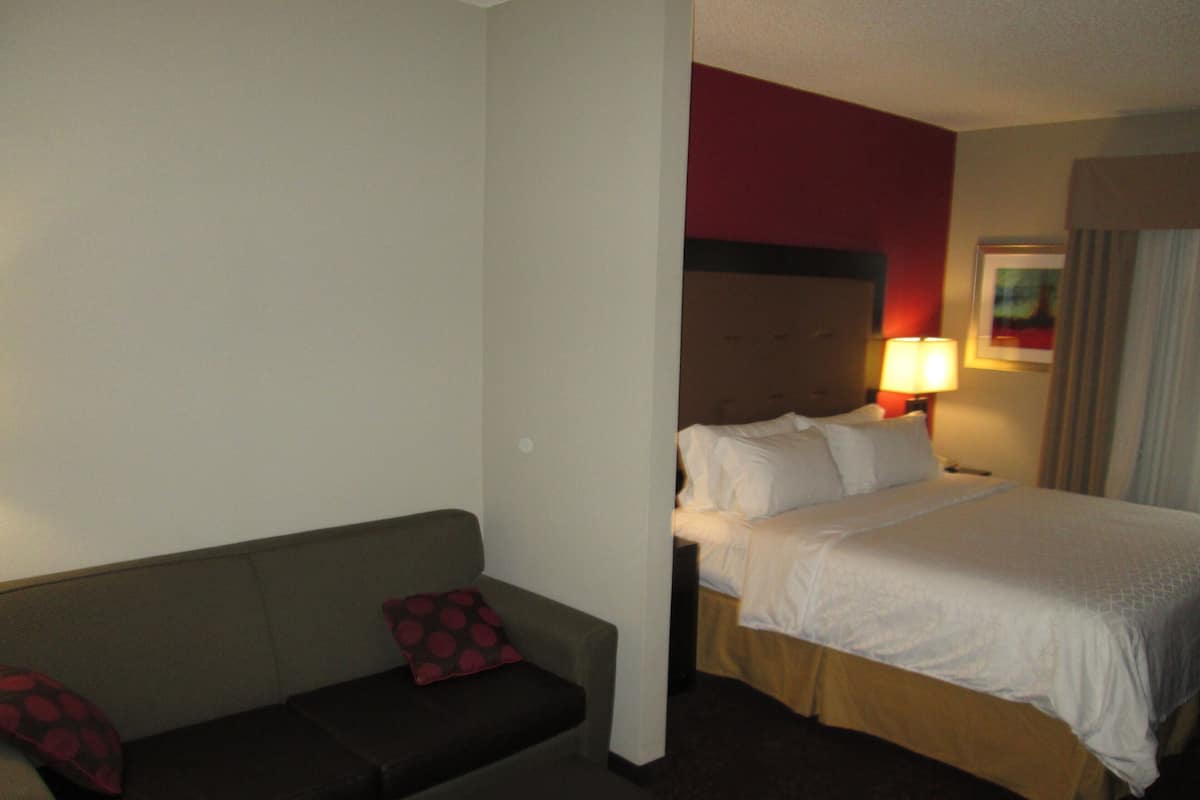 A hotel room with a bed, a sofa, and a nightstand with a lamp.