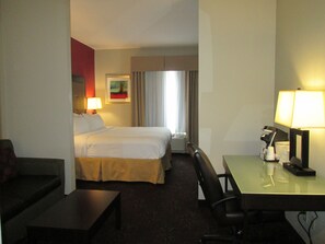 A hotel room with a bed, a desk, a chair, a lamp, and a painting on the wall.