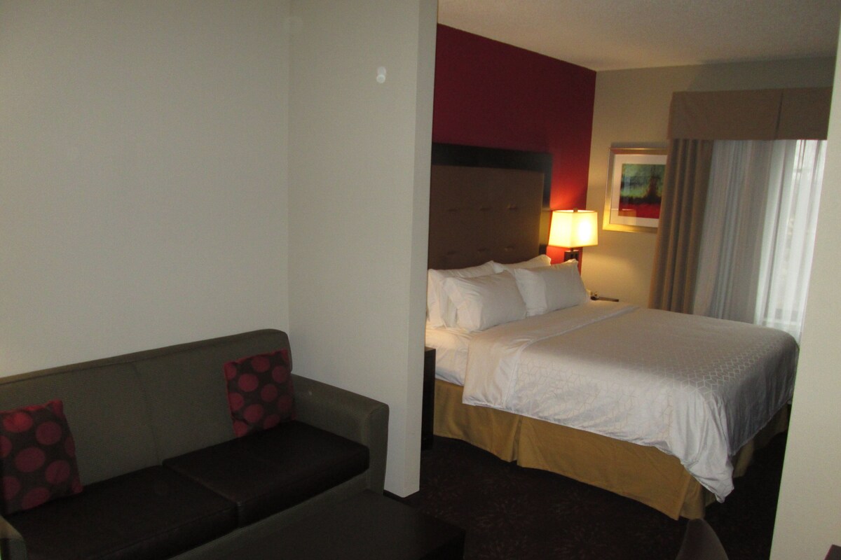 Una habitación de hotel con cama, sofá, mesita y un buró con lámpara.