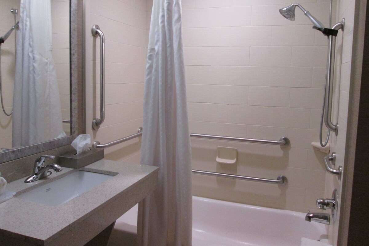 Un baño con ducha, barras de apoyo, lavamanos e inodoro.