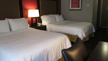 Une chambre d’hôtel avec deux lits, une table de chevet avec une lampe, un tableau encadré au mur et une chaise.