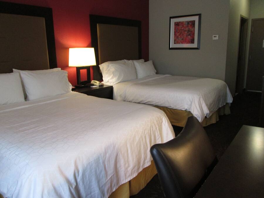Une chambre d’hôtel avec deux lits, une table de chevet avec une lampe, un tableau encadré au mur et une chaise.