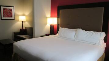 A hotel room with a large bed, two bedside tables, a nightstand, a lamp, and a framed picture on the wall.