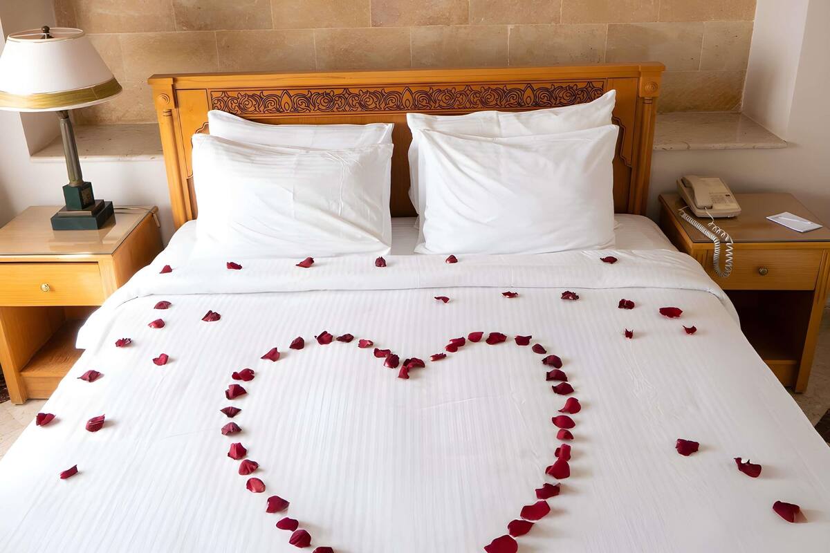 Habitación de hotel con una cama, dos almohadas, una lámpara de noche, un teléfono y un cuadro en la pared.