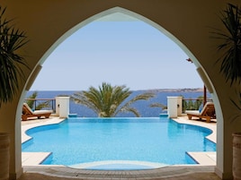 An infinity pool with a clear view of the sea, surrounded by lounge chairs and palm trees.