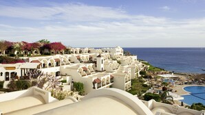 Un complex turístic amb edificis blancs, una piscina i vista al mar.