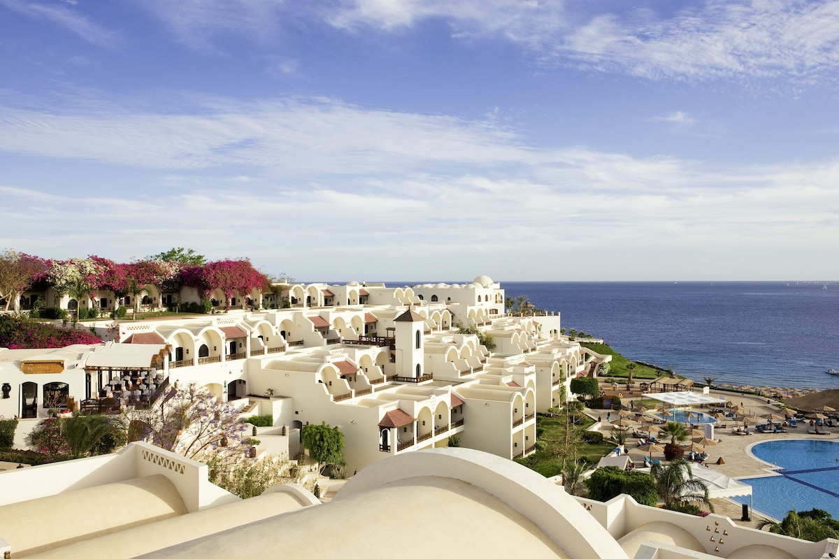 Un resort con edificios blancos, piscina y vista al mar.