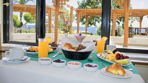 Taula de matí amb diversos plats, incloent fruita, pastissos i begudes, amb vista a una pèrgola de fusta i palmeres.