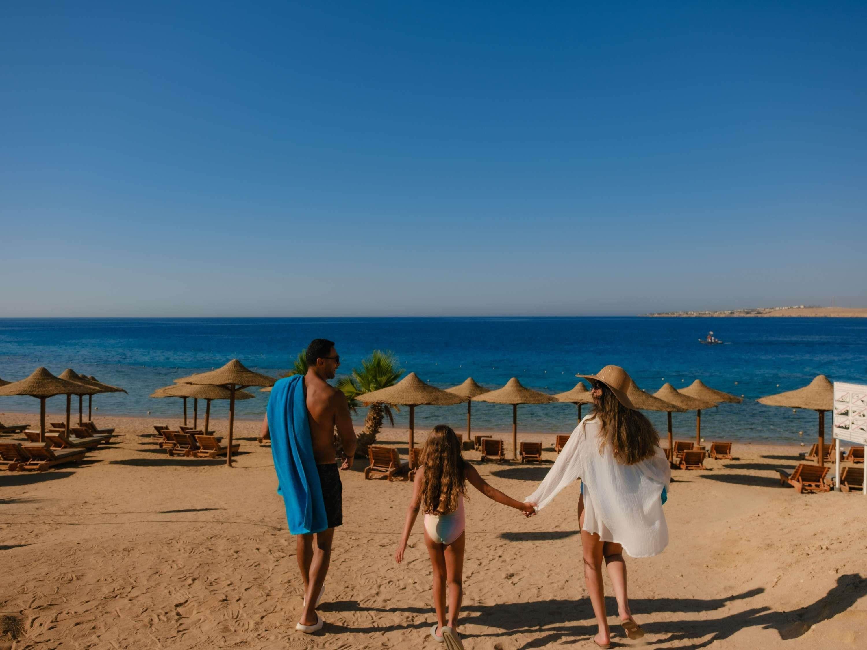 Une plage avec des transats et des parasols, un ciel bleu dégagé et la mer en arrière-plan.