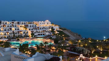 A resort with multiple white buildings, a swimming pool, and a view of the sea.