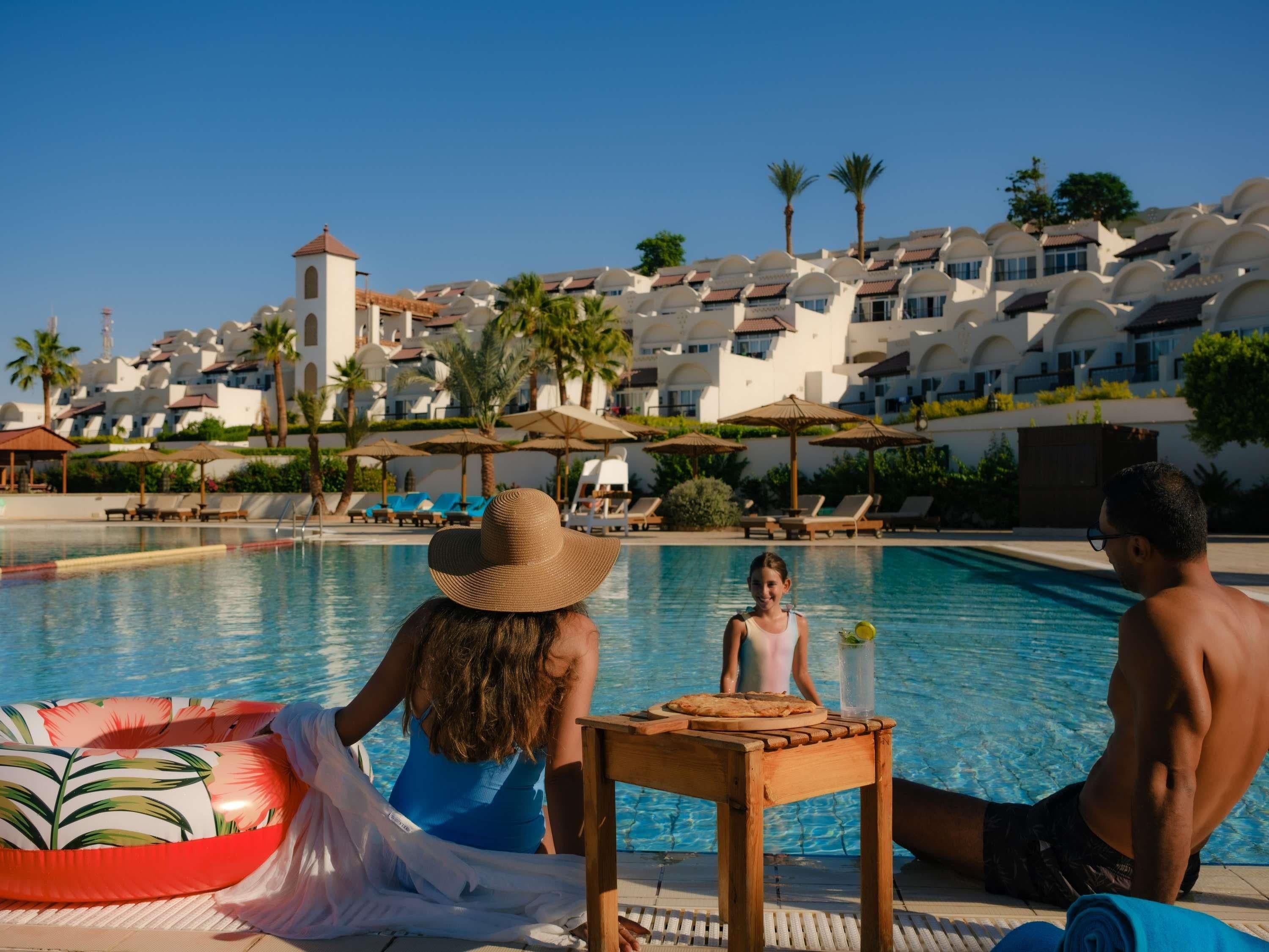 A poolside area with lounge chairs, umbrellas, and a view of a resort building with multiple balconies.
