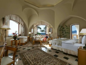 A spacious room with a large bed, a sofa, and a dining area. There are multiple windows providing views of the outdoors. - Mövenpick Resort Sharm El Sheik Naama Bay (Sharm El Sheikh)
