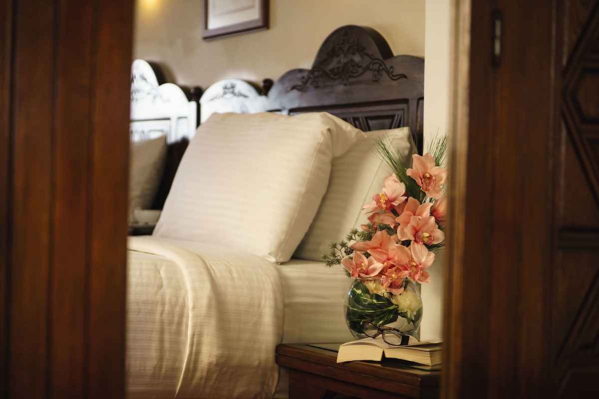 Un dormitorio con cama, una mesita de noche con un florero y un libro abierto.