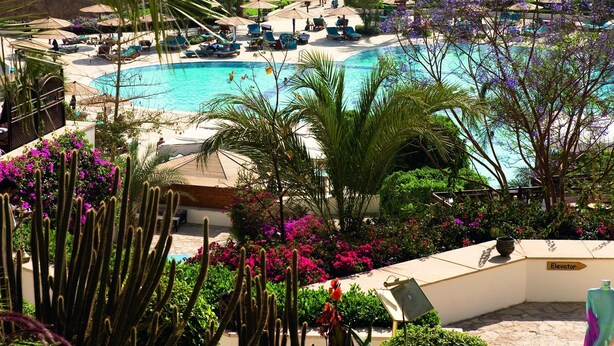A resort with a large pool, palm trees, and a view of the sea. - Mövenpick Resort Sharm El Sheik Naama Bay (Sharm El Sheikh)