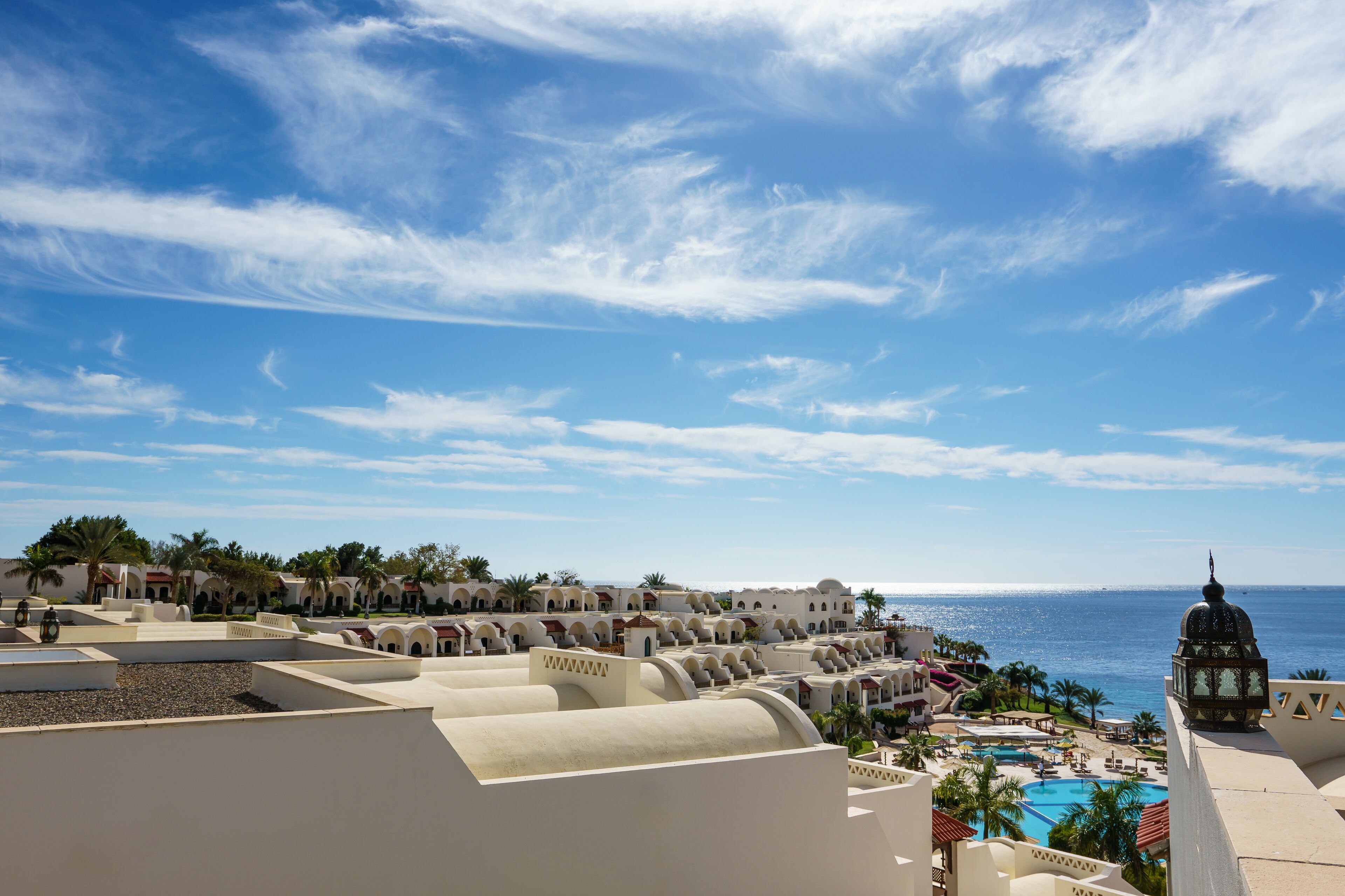 A resort with a pool, palm trees, and a view of the ocean.