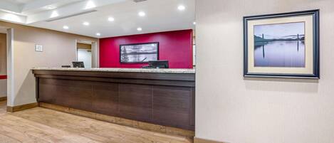 A reception area with a red accent wall, a framed picture, and a wooden floor.