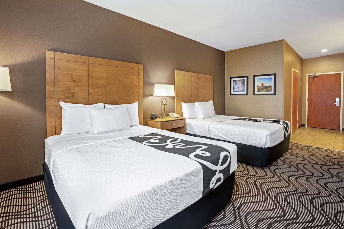 A hotel room with two beds, a nightstand, a lamp, and a door.