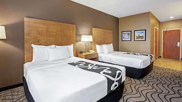 A hotel room with two beds, a nightstand, a lamp, and a door.