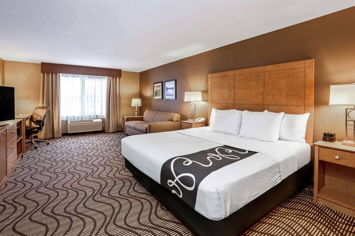 A hotel room with a large bed, a desk, a chair, a sofa, and a television.