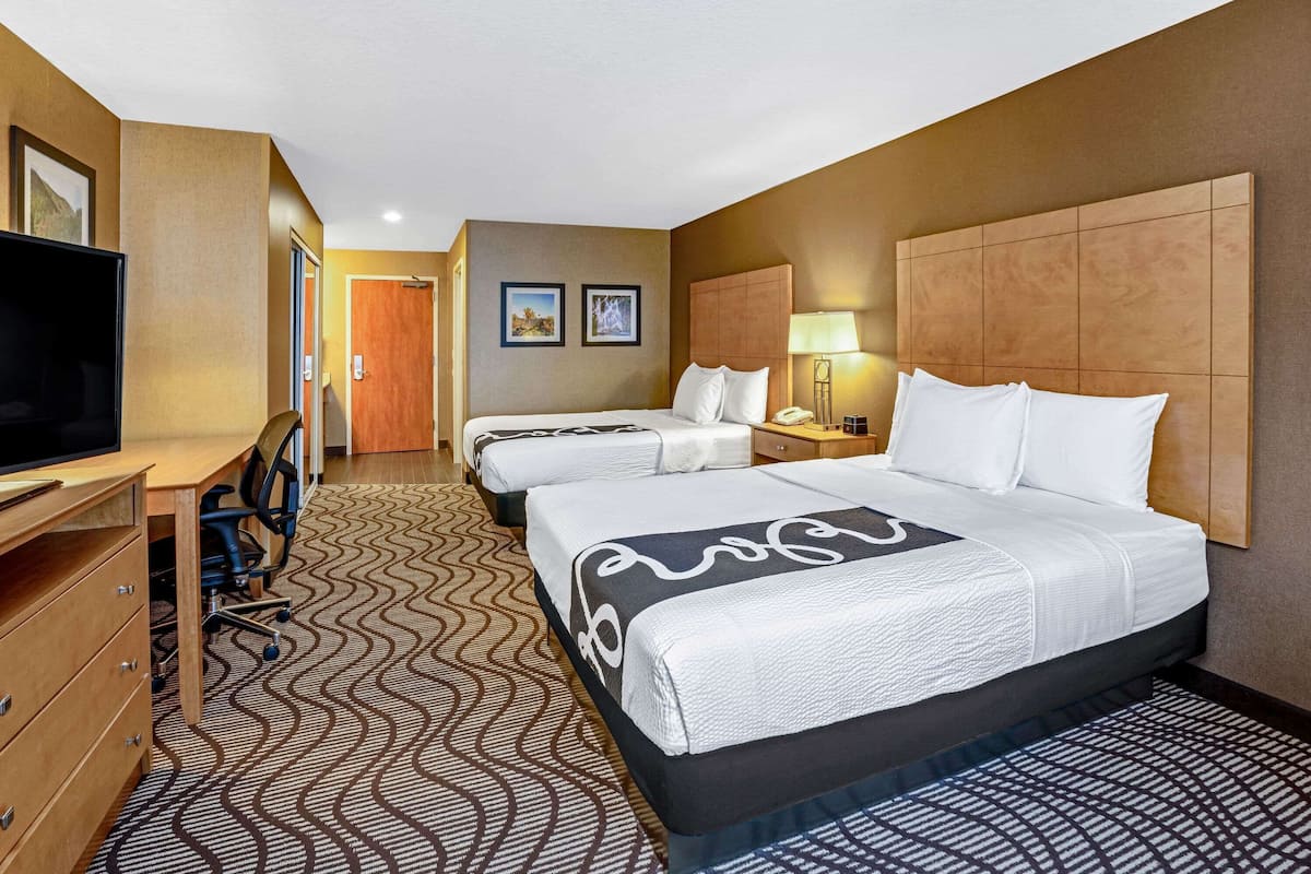A hotel room with two beds, a desk with a TV, and a patterned carpet.