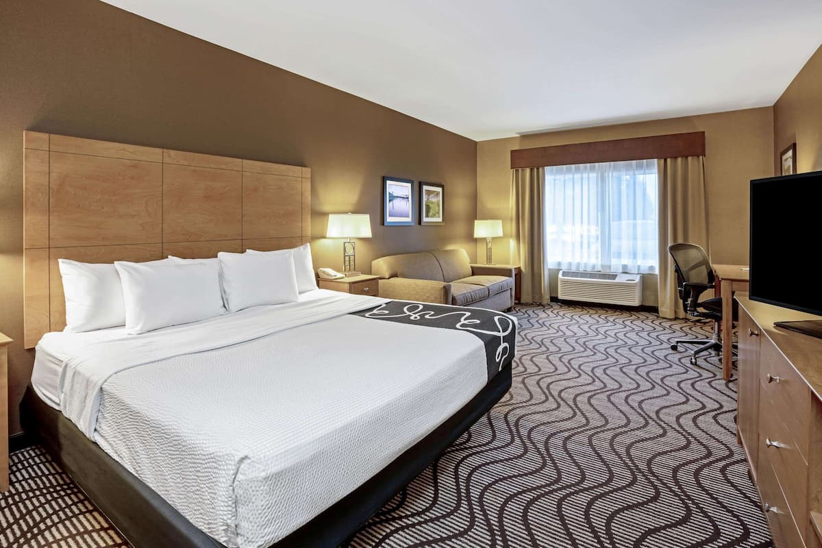 A hotel room with a large bed, a desk, a chair, a television, and a window with curtains.