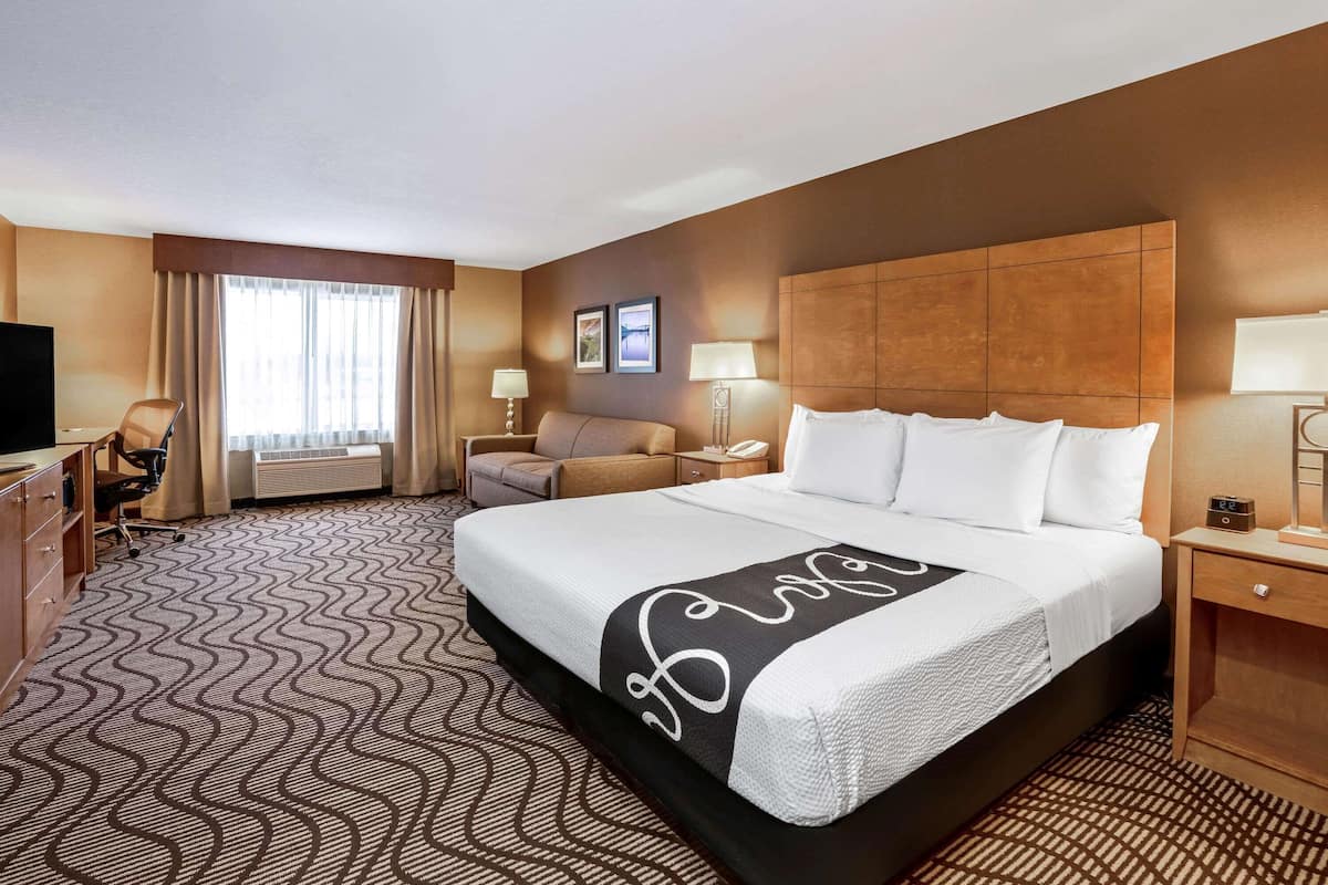A hotel room with a large bed, a desk with a chair, a TV, and a window with curtains.
