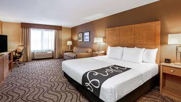 A hotel room with a large bed, a desk with a chair, a TV, and a window with curtains.