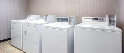 A laundry area with three white washing machines and dryers, a control panel, and a tiled floor.