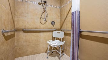 Un box de ducha accesible para sillas de ruedas con cabezal de ducha de mano, barras de apoyo y una silla blanca.