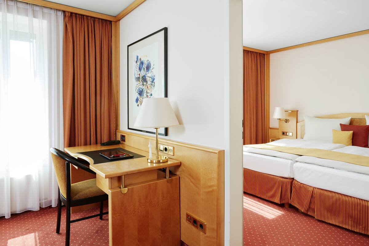 A hotel room with a desk, chair, bed, and artwork on the wall.