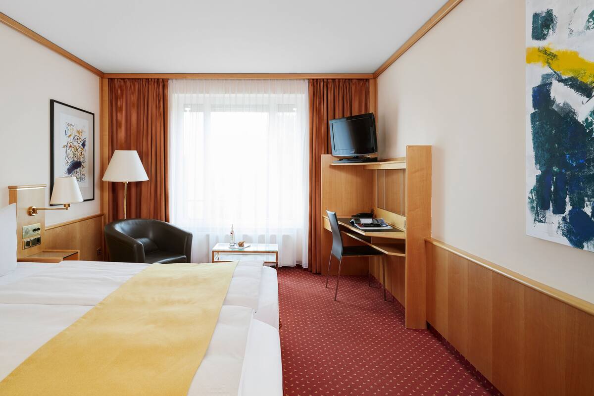 A hotel room with a bed, a desk, a chair, a television, and a window with curtains.