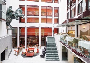 Un vestíbulo de hotel con una escalera central, zonas de estar y un bar.
