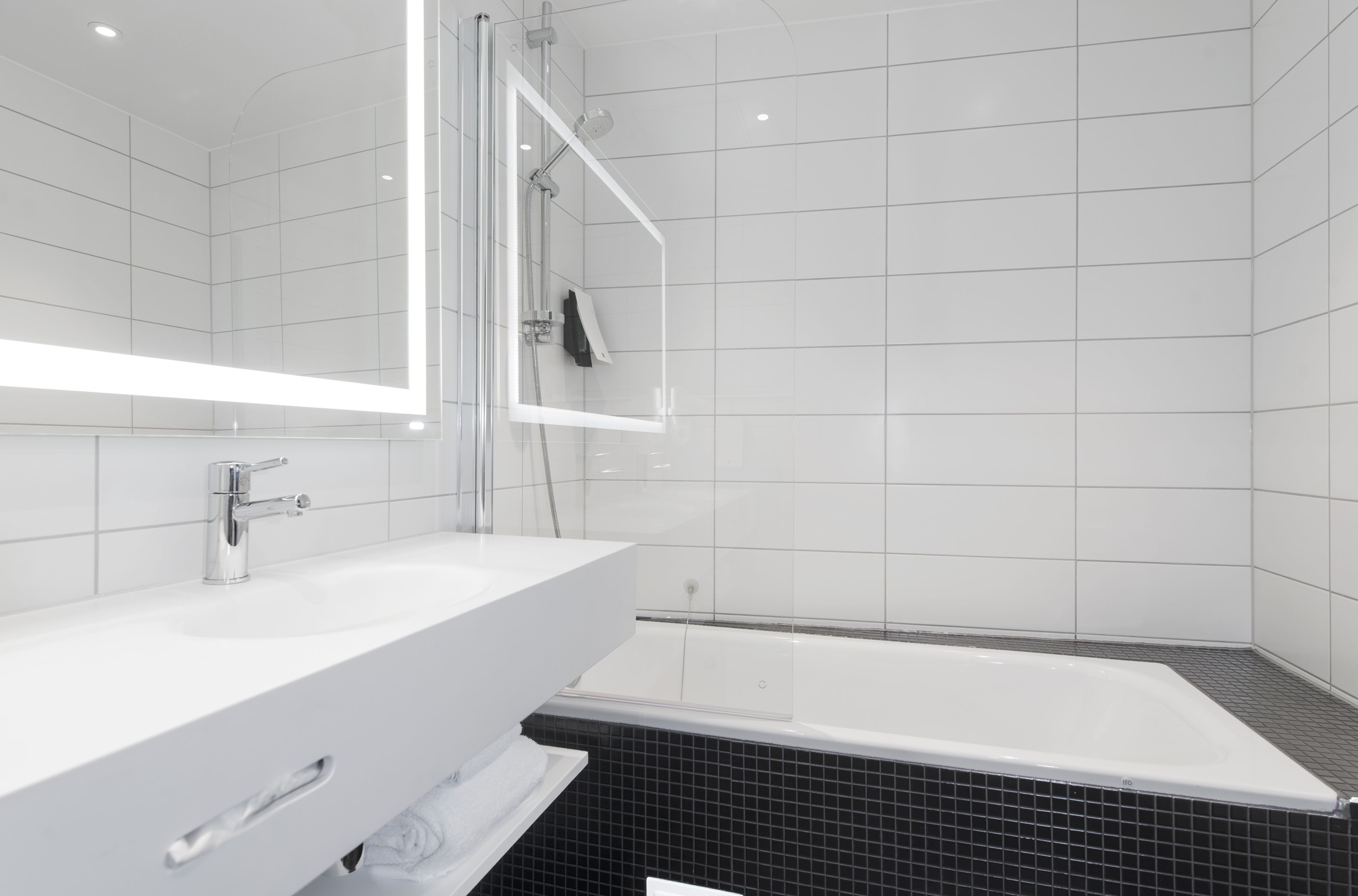 Et moderne badeværelse med et hvidt underskab, en glasafskærmet brusekabine og et sort flisegulv.