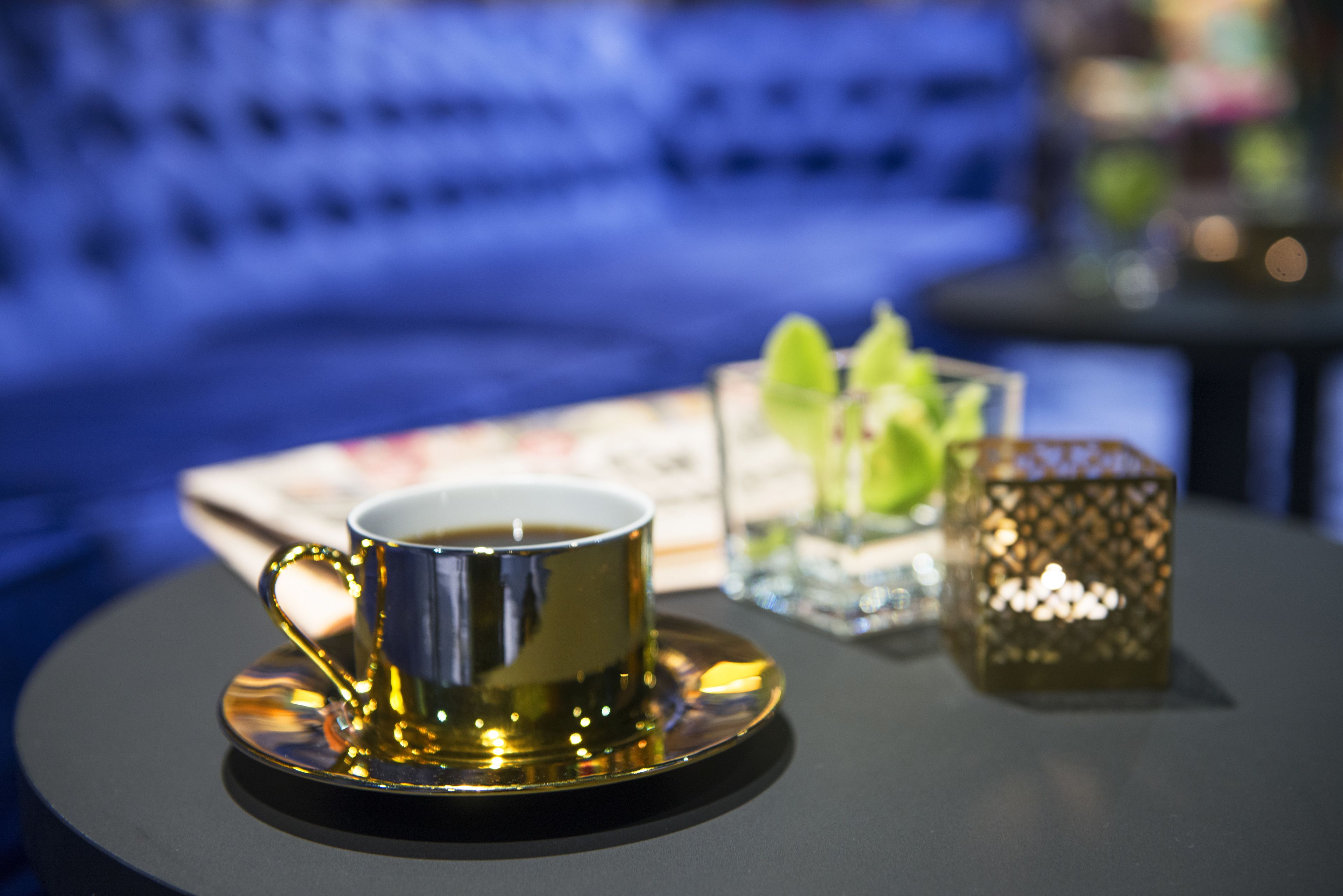 Eine Kaffeetasse auf Untertasse, ein kleines Glasgefäß mit Pflanze und ein dekorativer Laternen auf einem Tisch.