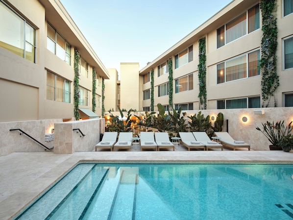 Una piscina al aire libre, sombrillas, sillones reclinables de piscina