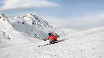 Une personne fait du ski sur une pente enneigée, avec une montagne en arrière-plan.