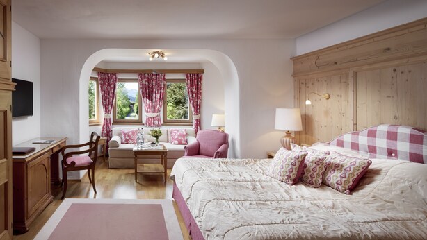 A bedroom with a large bed, a desk, a chair, and a window with curtains. - Relais & Châteaux Hotel Tennerhof (Kitzbuhel)