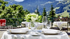A table set for two with white tablecloths, clear glassware, and a floral centerpiece, overlooking a mountainous landscape. - Relais & Châteaux Hotel Tennerhof (Kitzbuhel)