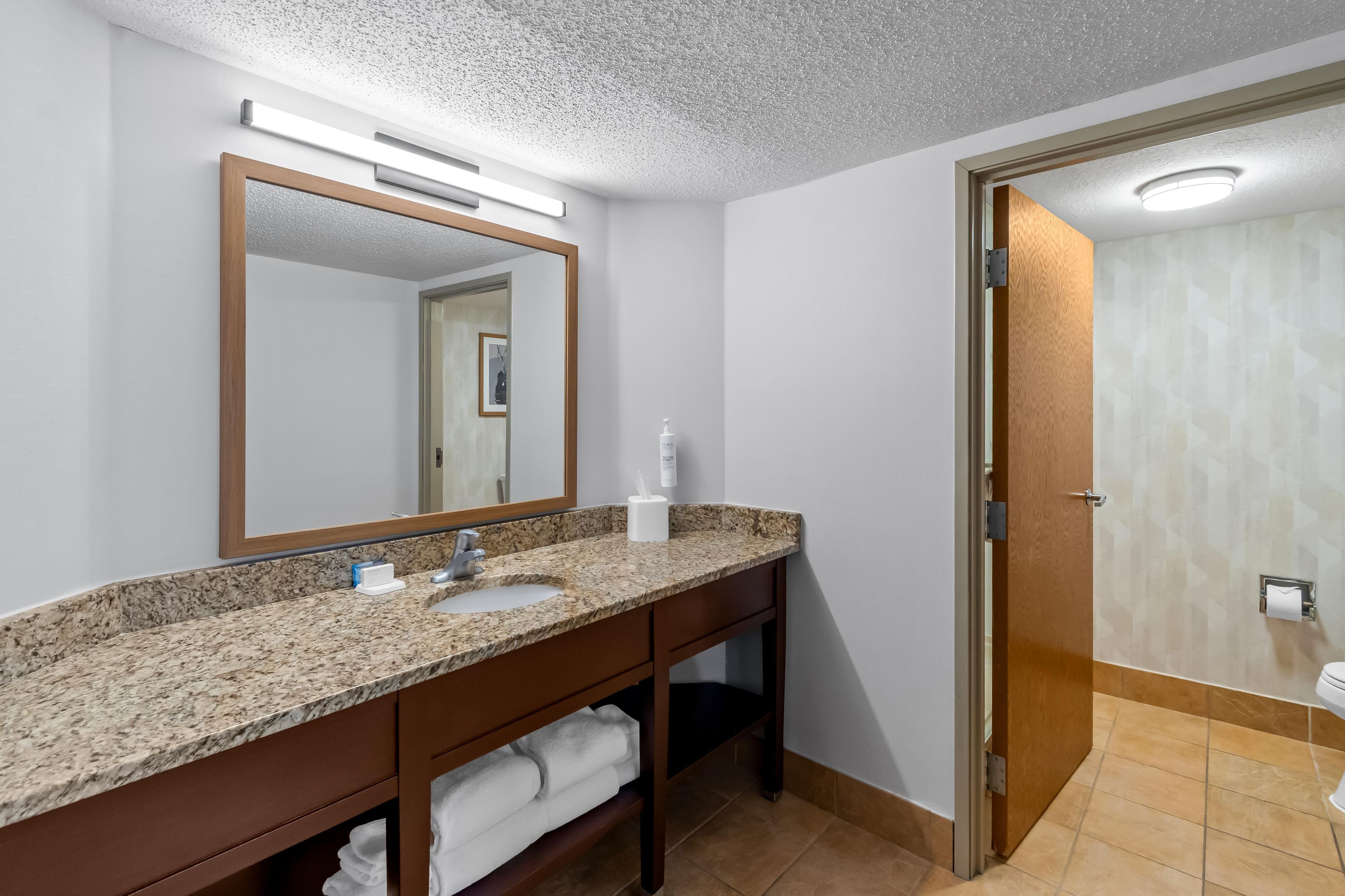 A bathroom with a granite countertop, a sink, a mirror, and a shower area.
