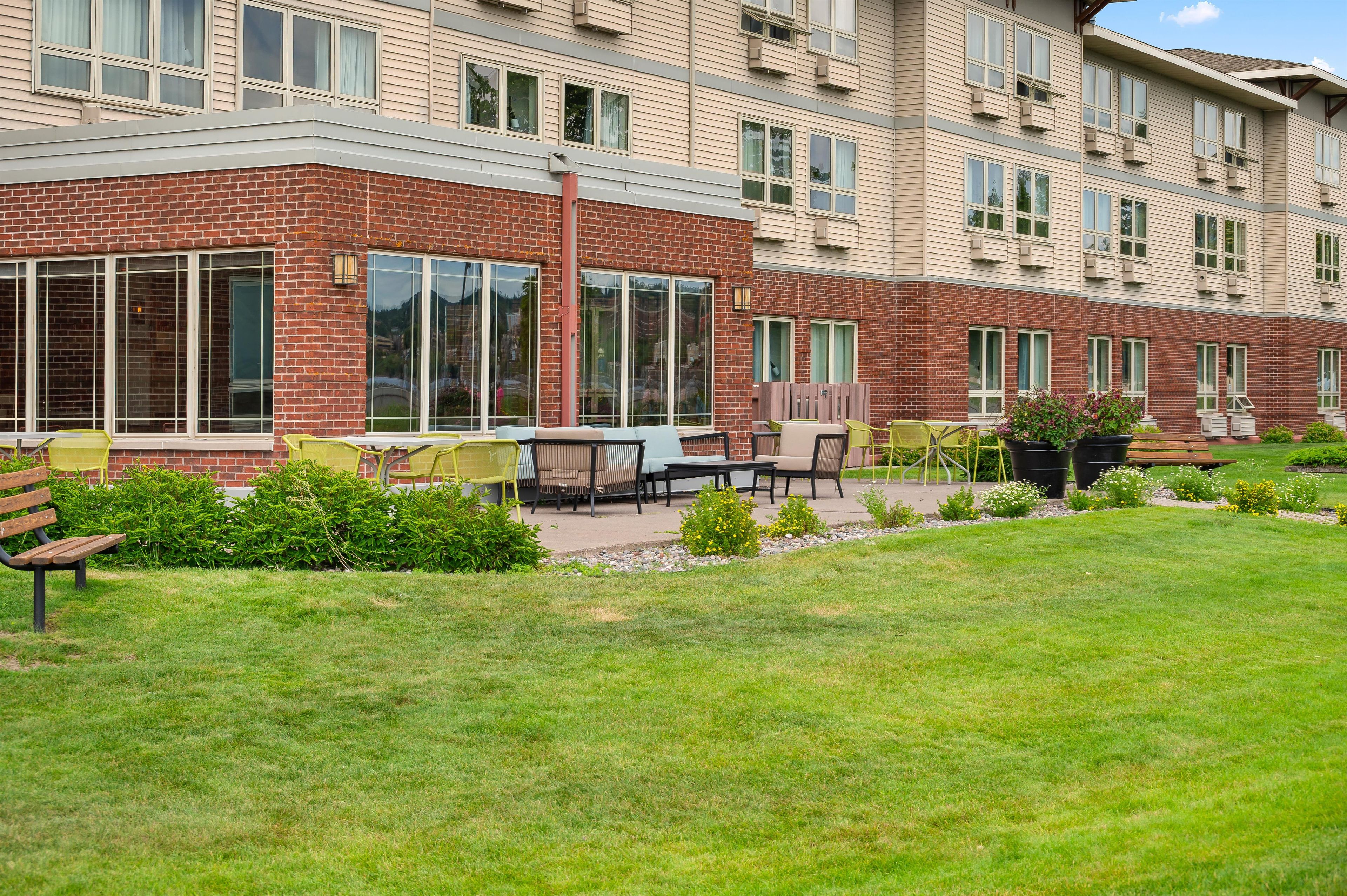 A multi-story residential building with a brick facade, large windows, and outdoor seating area with tables and chairs.