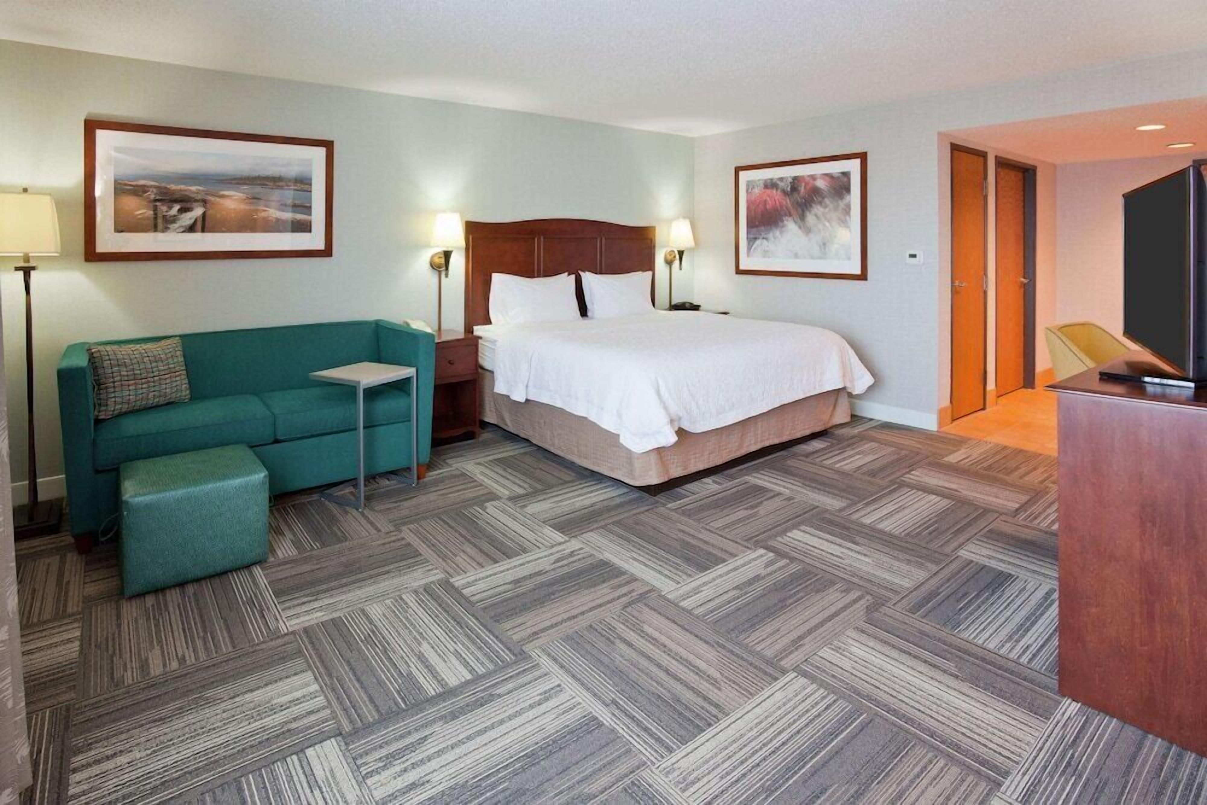 A hotel room with a bed, a sofa, a small table, a TV, and two framed pictures on the walls.
