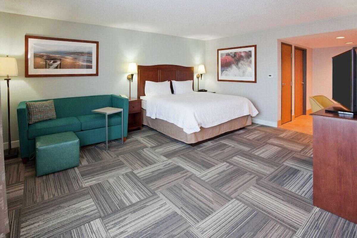 Habitación de hotel con cama, sofá, una mesita, televisor y dos cuadros en las paredes.