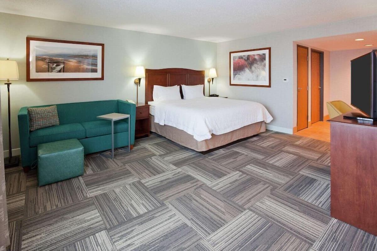A hotel room with a bed, a sofa, a small table, a TV, and two framed pictures on the walls.